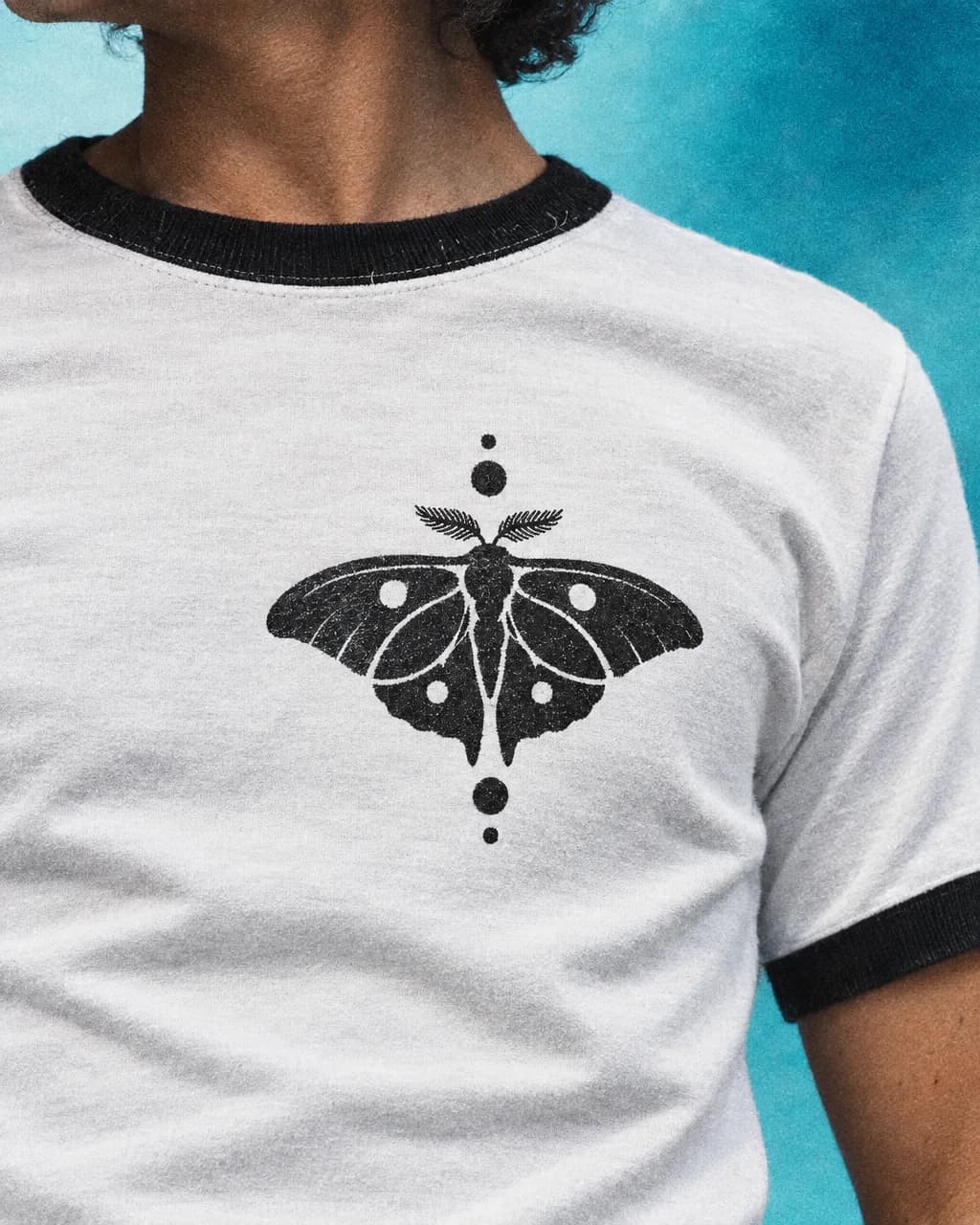 Close crop of a moth-and-dot print on the chest of a white ringer tee