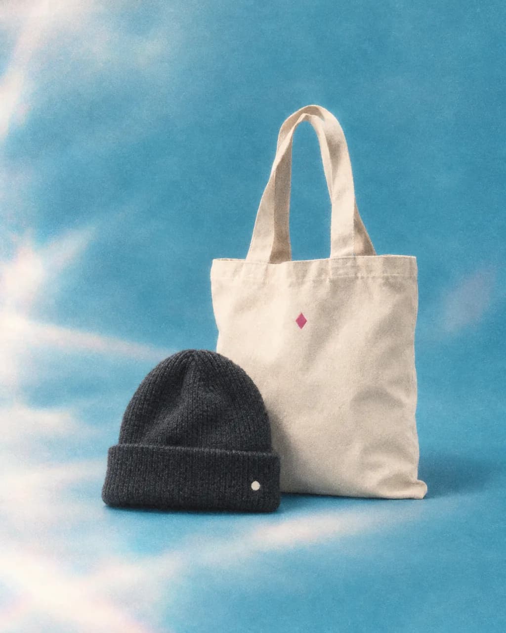 Charcoal beanie with a cream dot and a canvas tote with a magenta diamond on ice blue