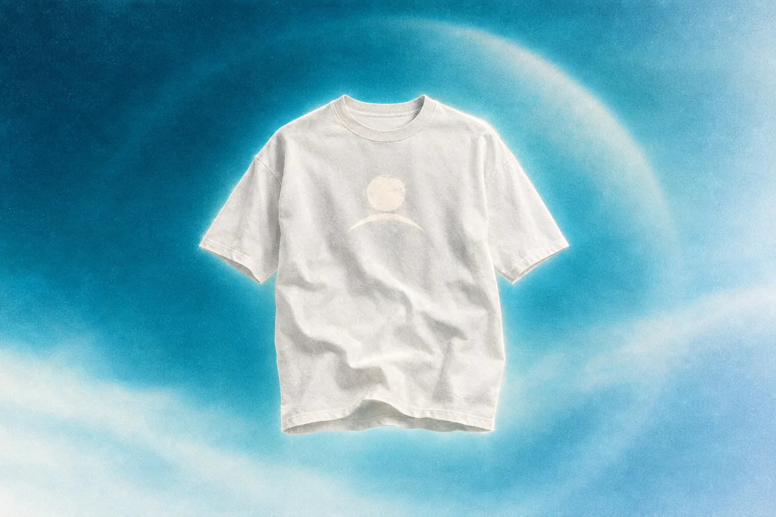 White t-shirt with a moon-and-arc chest print floating on a cyan atmospheric field