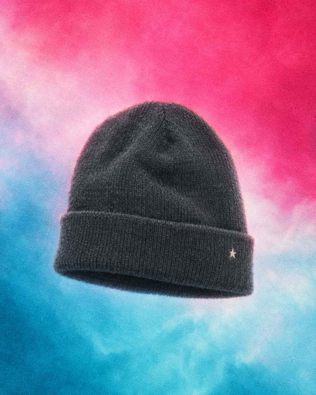 Charcoal knit beanie with a cream star on the cuff against a pink and cyan wash